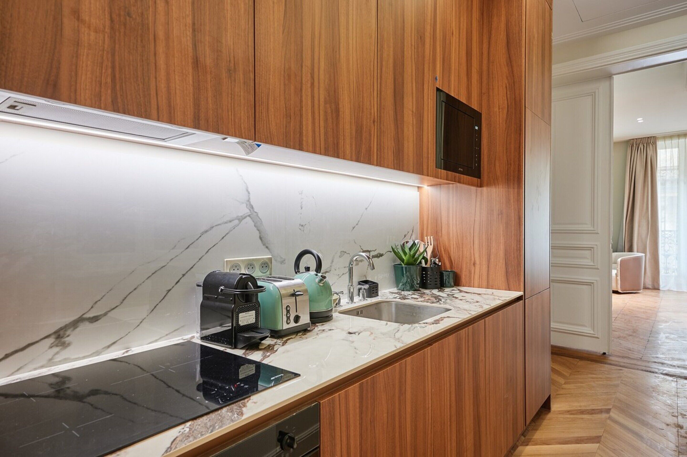 A modern kitchen with wooden cabinets, a marble countertop, and a built-in oven.