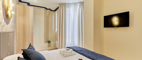 Ein Hotelzimmer mit einem Bett, einem an der Wand montierten Fernseher und einem Fenster mit Vorhängen.
