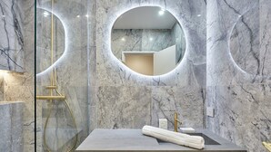 A bathroom with a marble wall, a round mirror, a shower, and a sink with a towel. - Sublime Flat in the Centre of Paris-montorgueil (Paris)