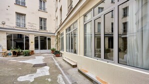 A courtyard with a building featuring large windows and a tiled floor. - Sublime Flat in the Centre of Paris-montorgueil (Paris)