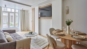 A modern living room with a sofa, a dining table set for four, and a TV mounted on the wall. - Sublime Flat in the Centre of Paris-montorgueil (Paris)