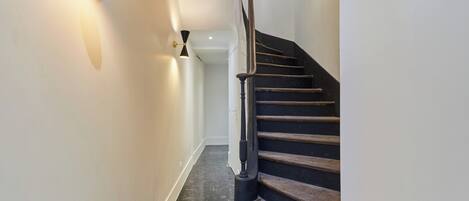 A modern staircase with a black handrail and wooden steps, leading to a landing with a white wall and a black floor.