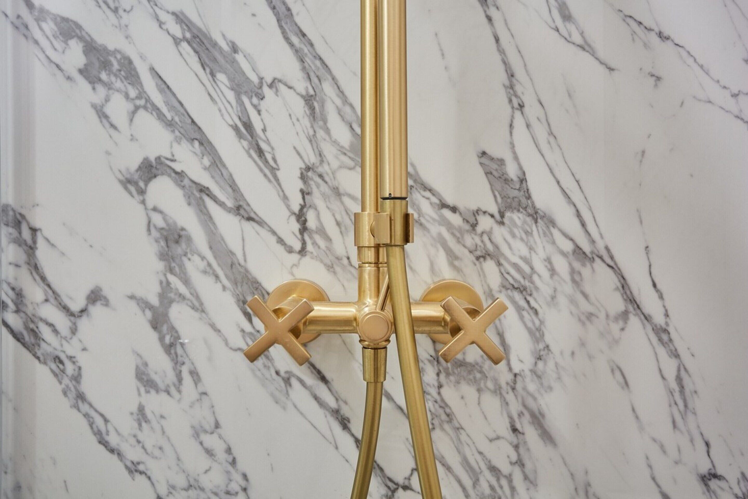 Gouden douchekop met twee kranen tegen een marmeren muur.