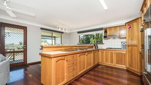 A kitchen with wooden cabinets, a central island, a built-in oven, and a window overlooking greenery. - Moore than a Shack - Ultimate coastal retreat (Guilderton)