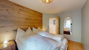 Un dormitorio con cabecera de madera, una cama grande con ropa de cama blanca, una mesita de noche con lámpara y un espejo en la pared.