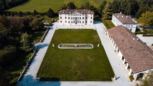 An aerial view of a large, symmetrical building with a central courtyard, surrounded by manicured lawns and trees. - Villa Solatia (Caldogno)
