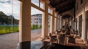A covered outdoor seating area with wicker furniture and a view of a building in the background. - Villa Solatia (Caldogno)