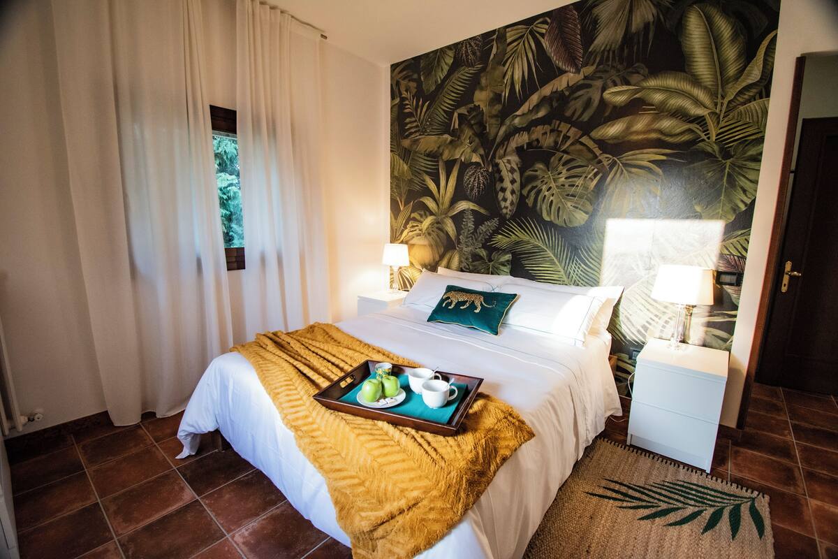 Une chambre d’hôtel avec un lit, une table de chevet, un plateau avec de la nourriture et une fresque murale représentant des feuilles tropicales.
