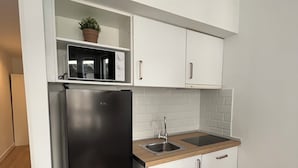 Una cocina compacta con un refrigerador negro, armarios blancos, una encimera de madera y una pequeña planta enmacorada en una repisa superior.