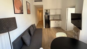 Un espacio habitable compacto con sofá, una mesa de comedor, televisor, zona de cocina y obras de arte en las paredes.