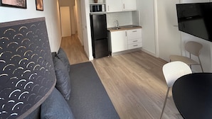 Una cocina moderna con armarios blancos, un refrigerador negro y un microondas. Hay un comedor con una mesa negra y sillas blancas.