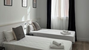 Habitación de hotel con dos camas individuales, una mesita de noche y una ventana con cortinas negras.