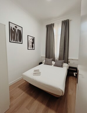 Ein ordentlich eingerichtetes Schlafzimmer mit einem Bett, Kissen und zwei gerahmten Kunstwerken an der Wand.
