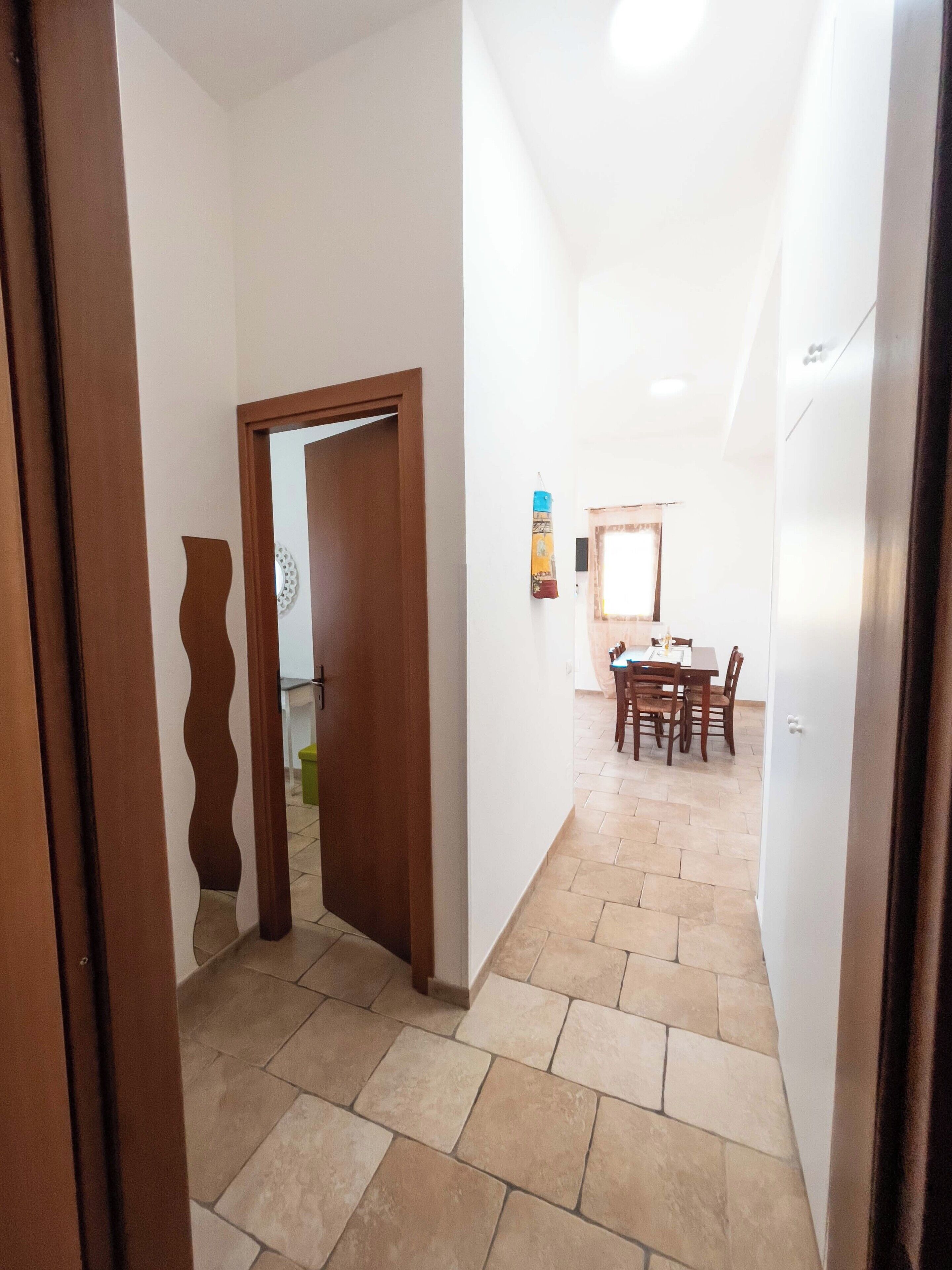 A hallway with a wooden door, a dining area with a table and chairs, and a window with curtains.