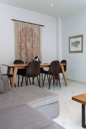A modern dining area with a wooden table and brown chairs, a beige sofa, and a framed artwork on the wall.