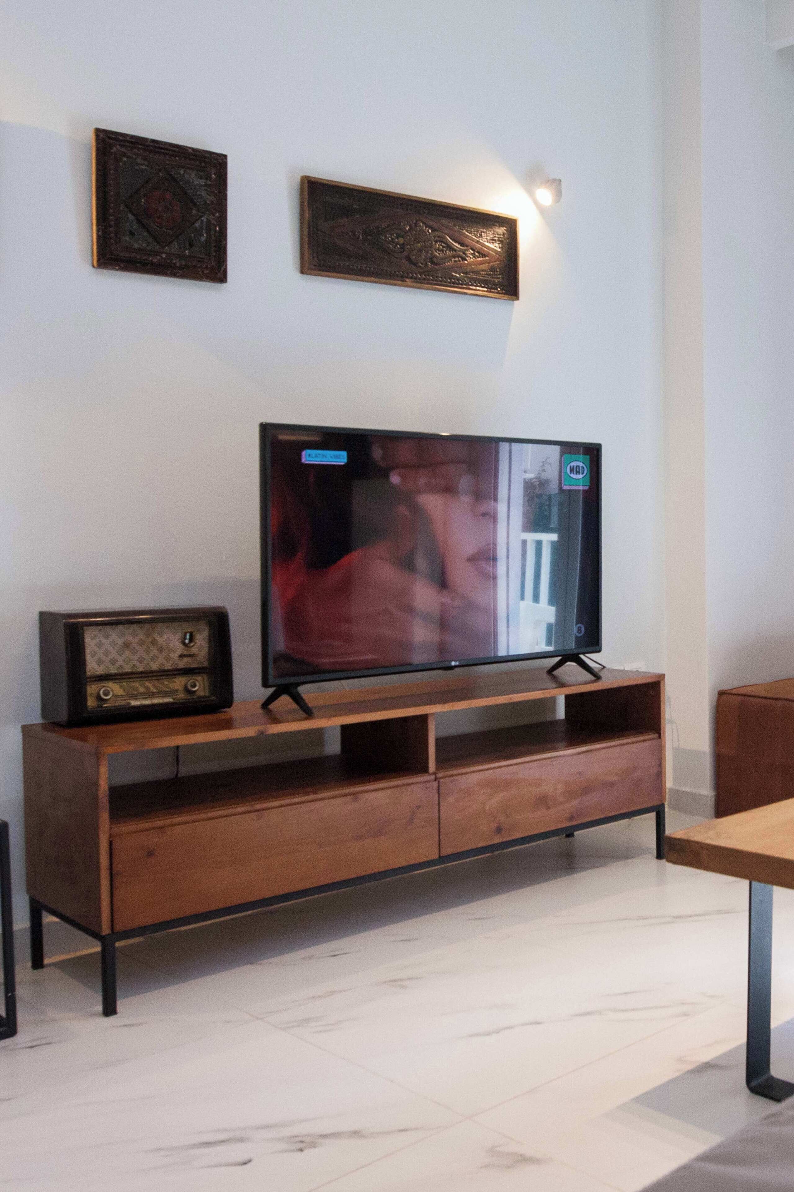 Uma sala de estar moderna com um móvel de entretenimento de madeira, uma TV de tela plana e dois quadros pendurados na parede.