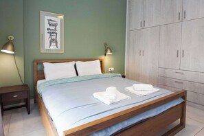 A neatly made bed with white linens and two towels, a wooden headboard, a framed picture on the wall, and a wardrobe with multiple doors.