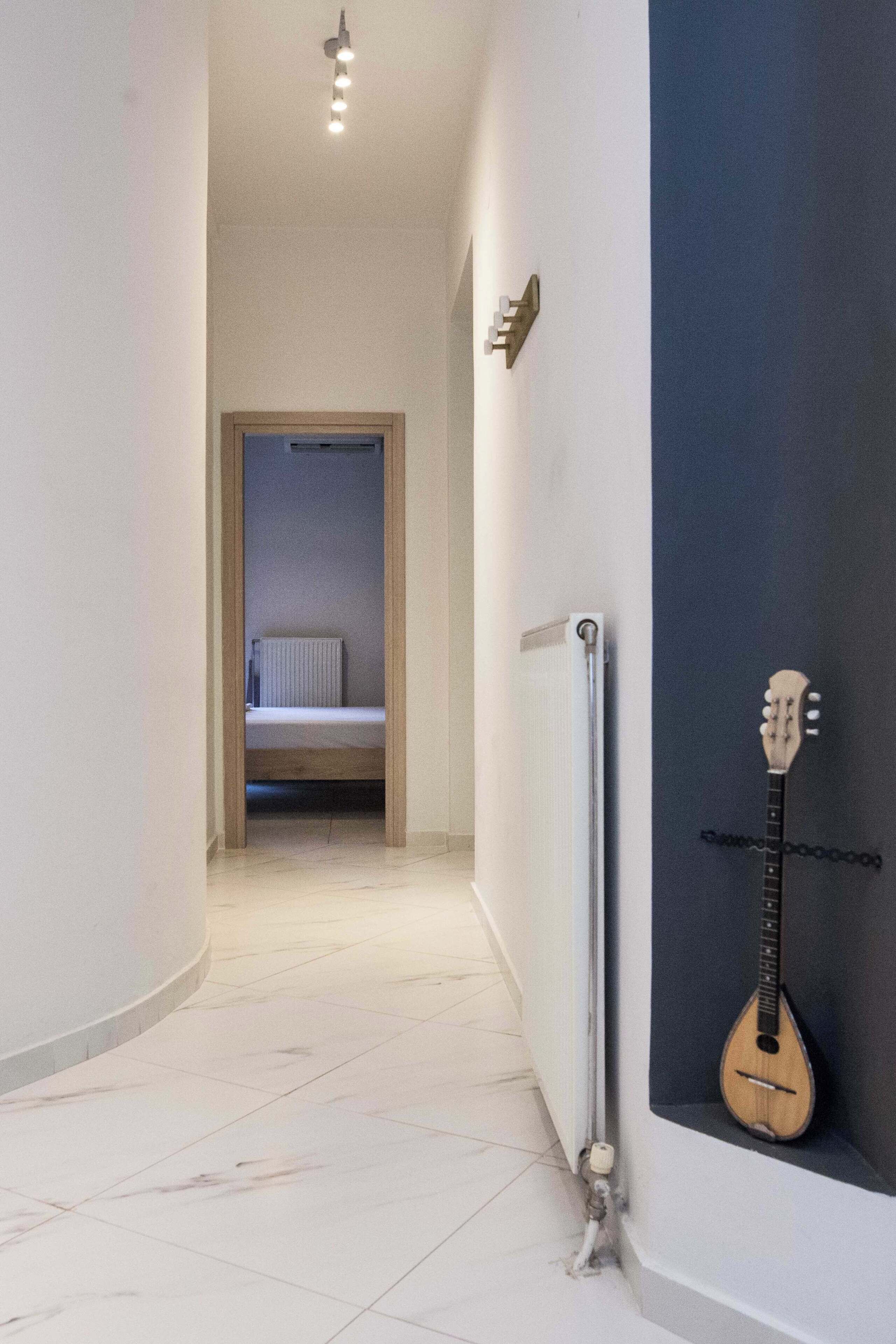 A narrow hallway with a radiator, a bed in the background, and a guitar leaning against a dark wall.