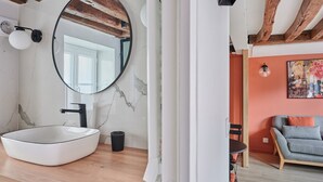 A bathroom with a large oval sink, a round mirror, and a wooden ceiling. - Charming Studio Center of Paris-montorgueil (Paris)