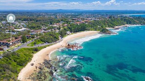 An aerial view of a coastal area with a beach, rocky shoreline, and residential buildings.