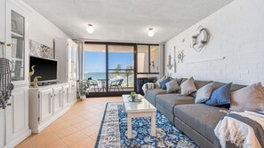 A living room with a sofa, coffee table, and a view of the sea through a glass door. - Beachpark 11 - Charming 2-bedroom holiday unit (Port Macquarie)