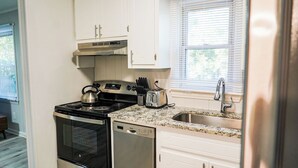 Una cocina con armarios blancos, estufa de acero inoxidable, lavavajillas y encimera de granito.