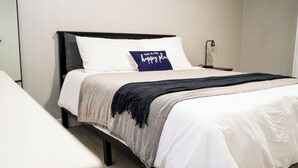 Una cama bien hecha con un almohadón azul, una manta estampada y un cabecero negro.