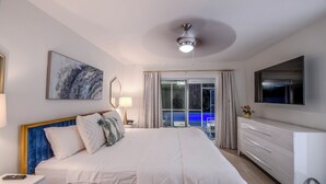 A hotel room with a large bed, a ceiling fan, a TV, and a view of the pool through the glass door.