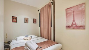 A neatly made bed with a brown blanket, a white pillow, and a rolled towel. There are three framed pictures on the wall. - Superb Atypical Apartment Paris Center Le Marais (Paris)