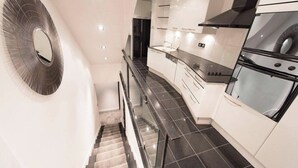 A modern kitchen with a central island, black tiled flooring, and white cabinetry. - Superb Atypical Apartment Paris Center Le Marais (Paris)