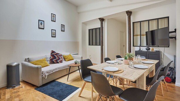 A modern living room with a dining area, featuring a sofa, coffee table, and a wooden dining table set for four. - Superb Atypical Apartment Paris Center Le Marais (Paris)