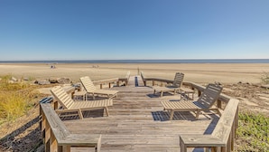 Eine Holzterrasse mit Liegestühlen, die auf einen Strand blickt.