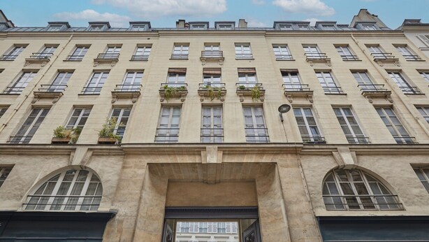 Un edificio a più piani con facciata simmetrica, ampie finestre e balconi adornati da piante.