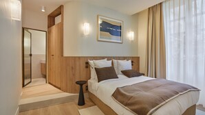 Camera d'albergo moderna con un letto grande, pannelli in legno, un quadro sopra il letto e vista sull'esterno attraverso tende leggere.