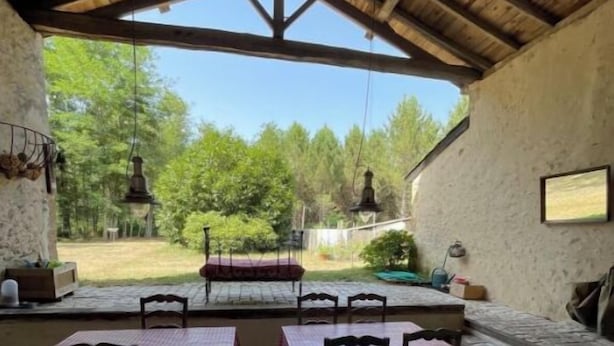 An outdoor patio with stone flooring, wooden tables with checkered tablecloths, and hanging lanterns.