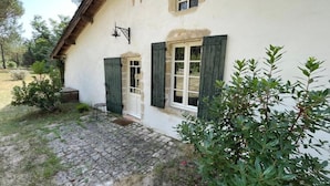 A rustic house with a cobblestone entrance, a small porch, and a garden with shrubs.