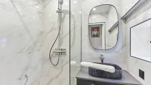 Une salle de bain moderne avec une douche à parois de verre, un mur recouvert de carreaux de marbre, un lavabo en marbre noir et un grand miroir.