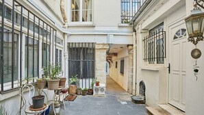 Un patio estrecho con plantas en macetas, una silla de metal y una puerta blanca.
