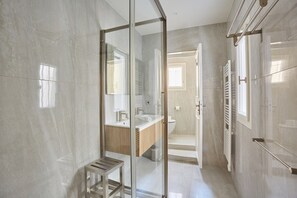 Ein modernes Badezimmer mit einer Glaskabine zur Dusche, einer Holzbank sowie einem sichtbaren Bereich für Toilette und Waschbecken.