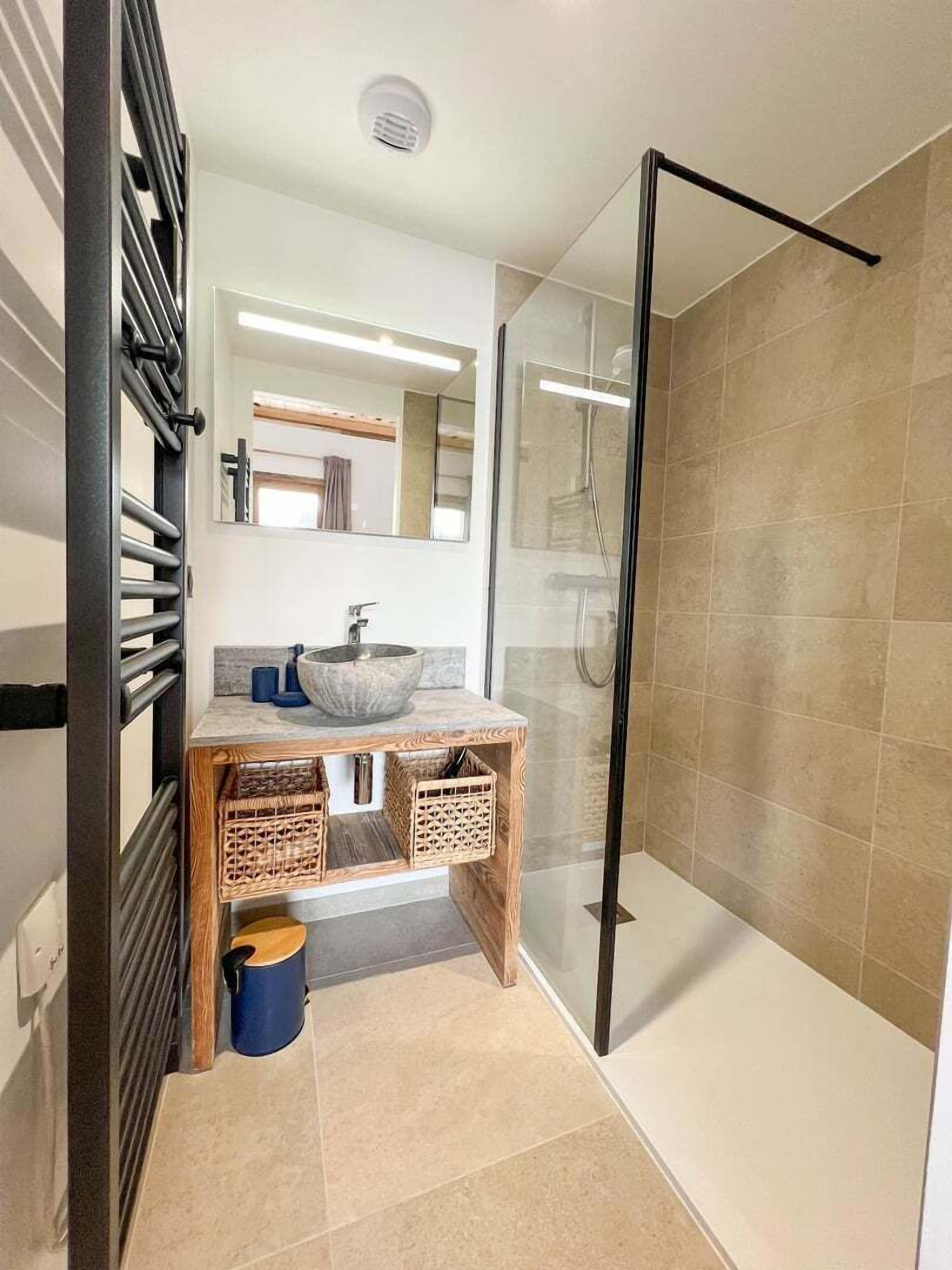 Ein modernes Badezimmer mit einer Duschkabine aus Glas, einem Holzausleger mit einem Aufsatzbecken und einem Spiegel darüber.
