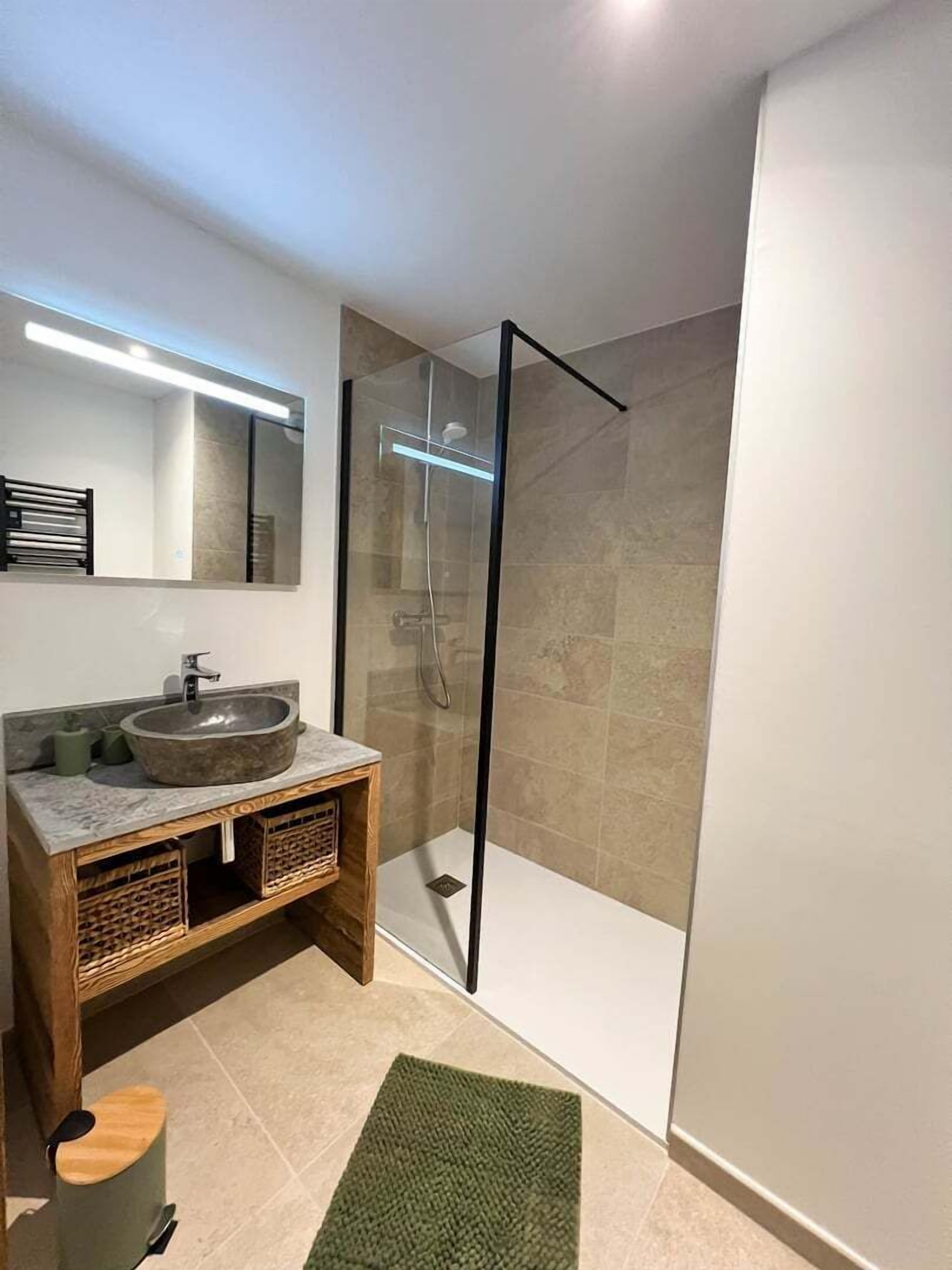 Ein modernes Badezimmer mit einer gläsernen Dusche, einem Holzbadezimmer-Möbel mit einem großen Waschbecken und einem Spiegel darüber.