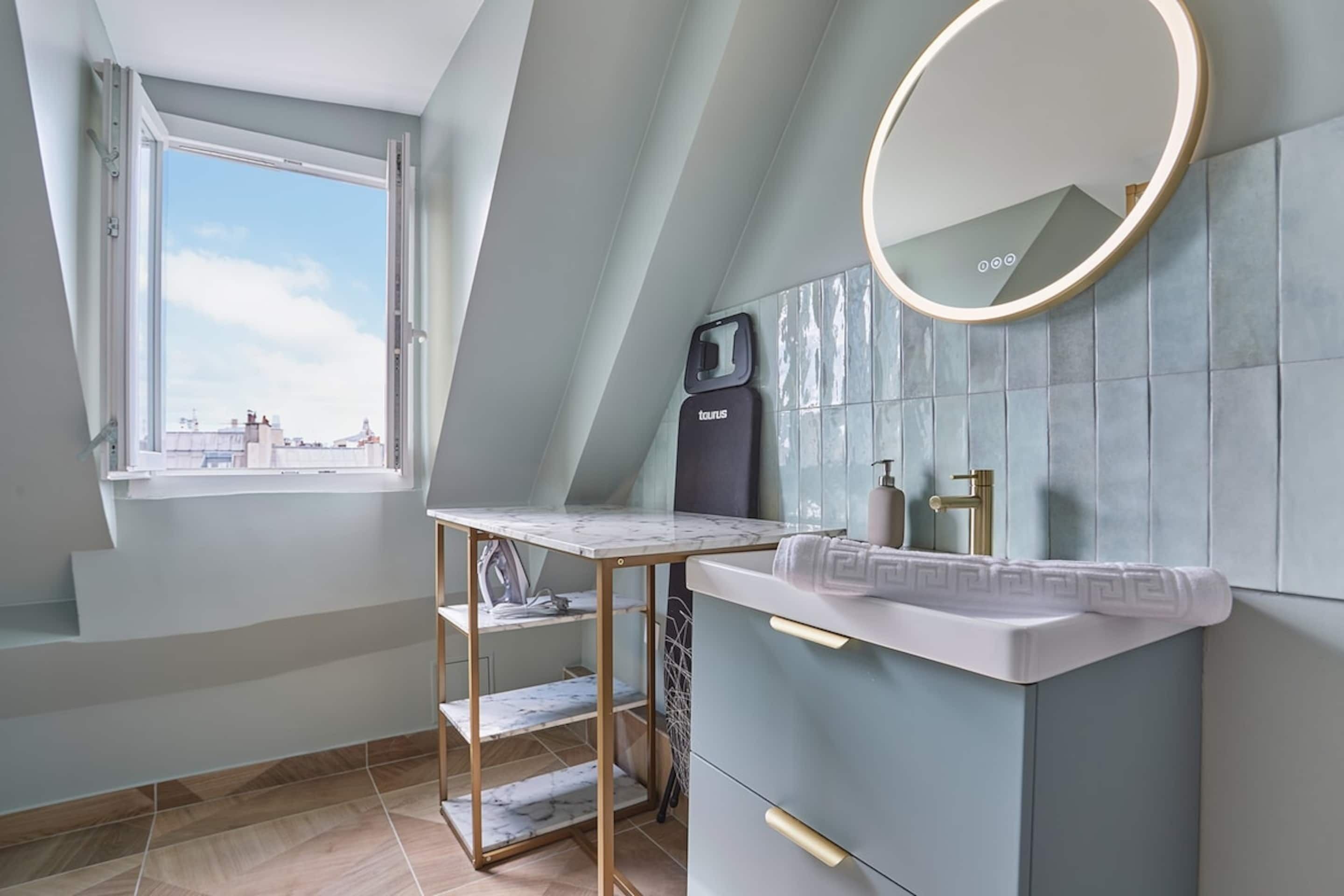 A modern bathroom with a marble vanity, a round mirror, and a window with a view of buildings.