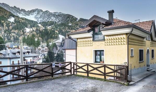 Un bâtiment jaune à l’architecture traditionnelle, une clôture en bois et un paysage montagneux en arrière-plan.