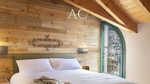 A bedroom with a wooden headboard, a bed with white bedding, a nightstand, a wall-mounted lamp, and a window with a view of a balcony. - Olivia s Home in Ponte di Legno (Ponte di Legno)