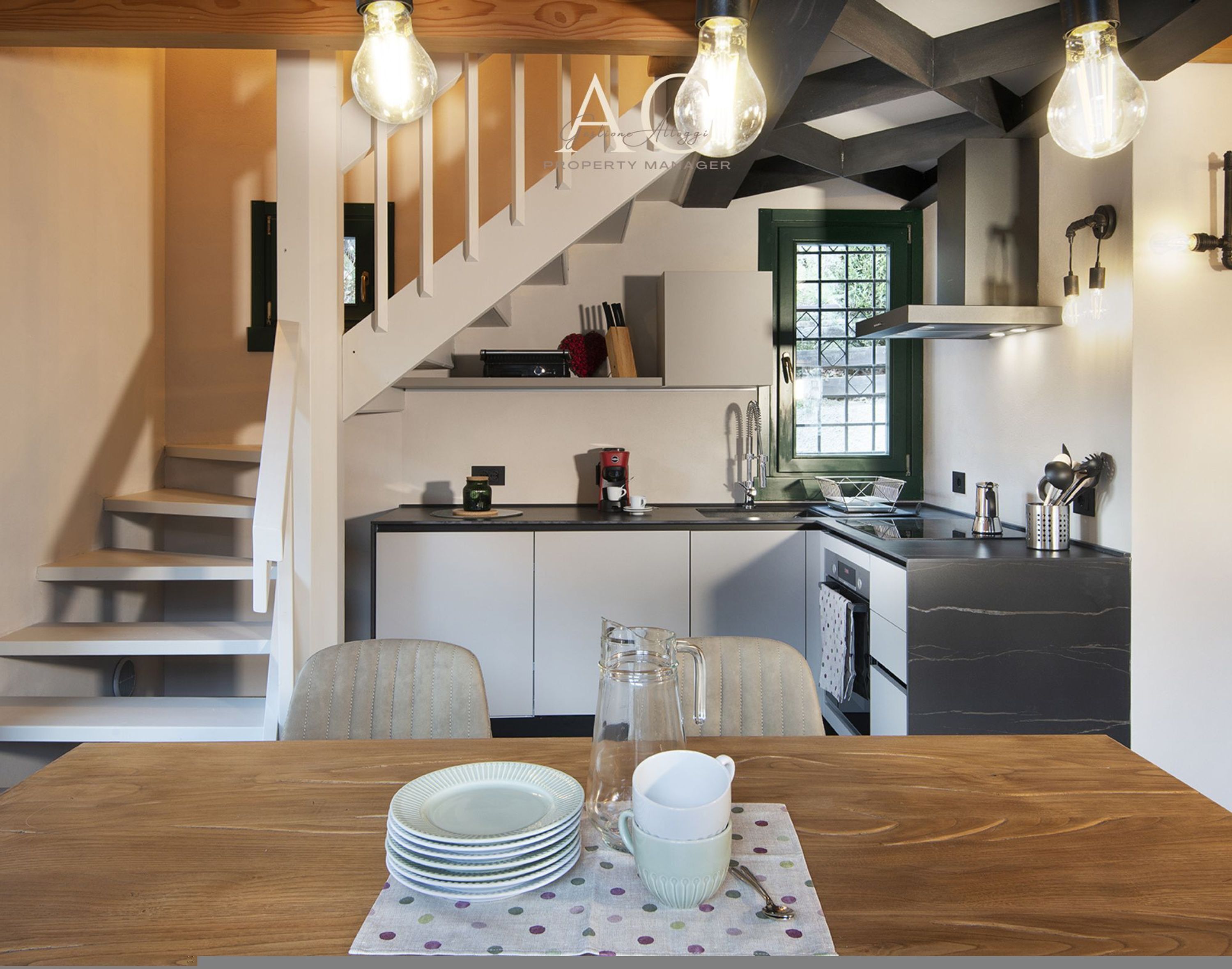 A modern kitchen with a wooden staircase, a dining table with plates and cups, and a coffee maker.