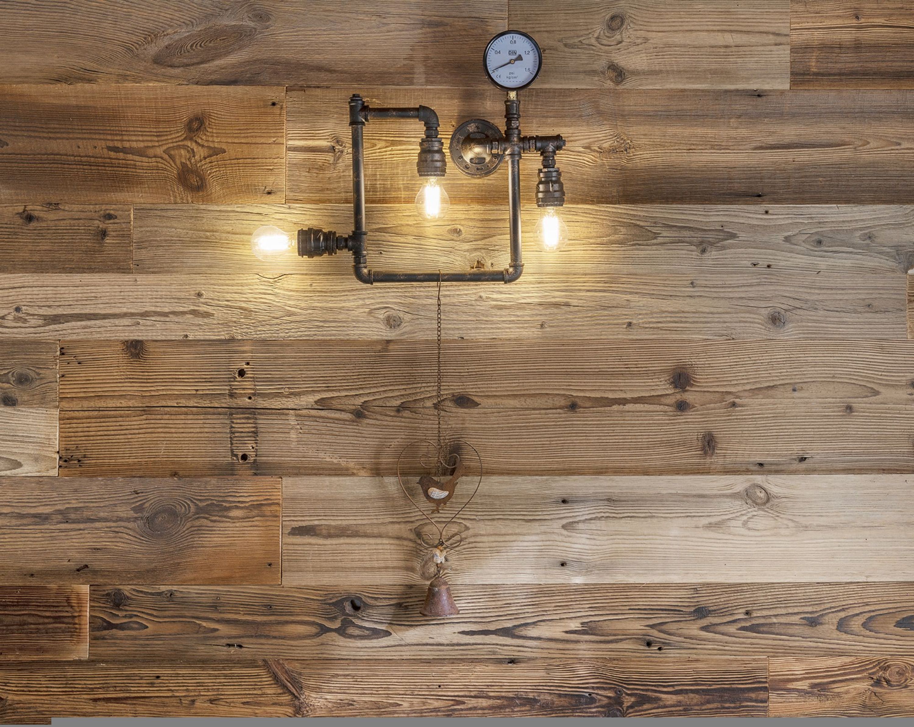 Un mur en bois agrémenté d’un luminaire de style rétro, avec des tuyaux apparents et un manomètre.