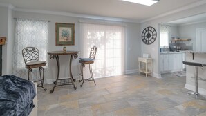 A spacious living area with a dining table, two chairs, a small side table, and a kitchen area with a bar stool.