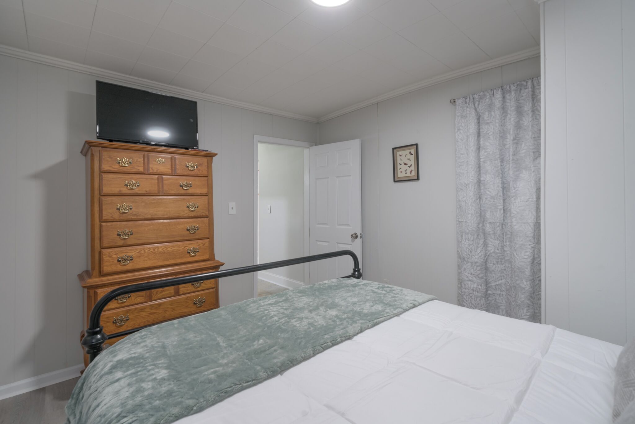 A bedroom with a bed, a wooden dresser, a television on top, and a door in the background.
