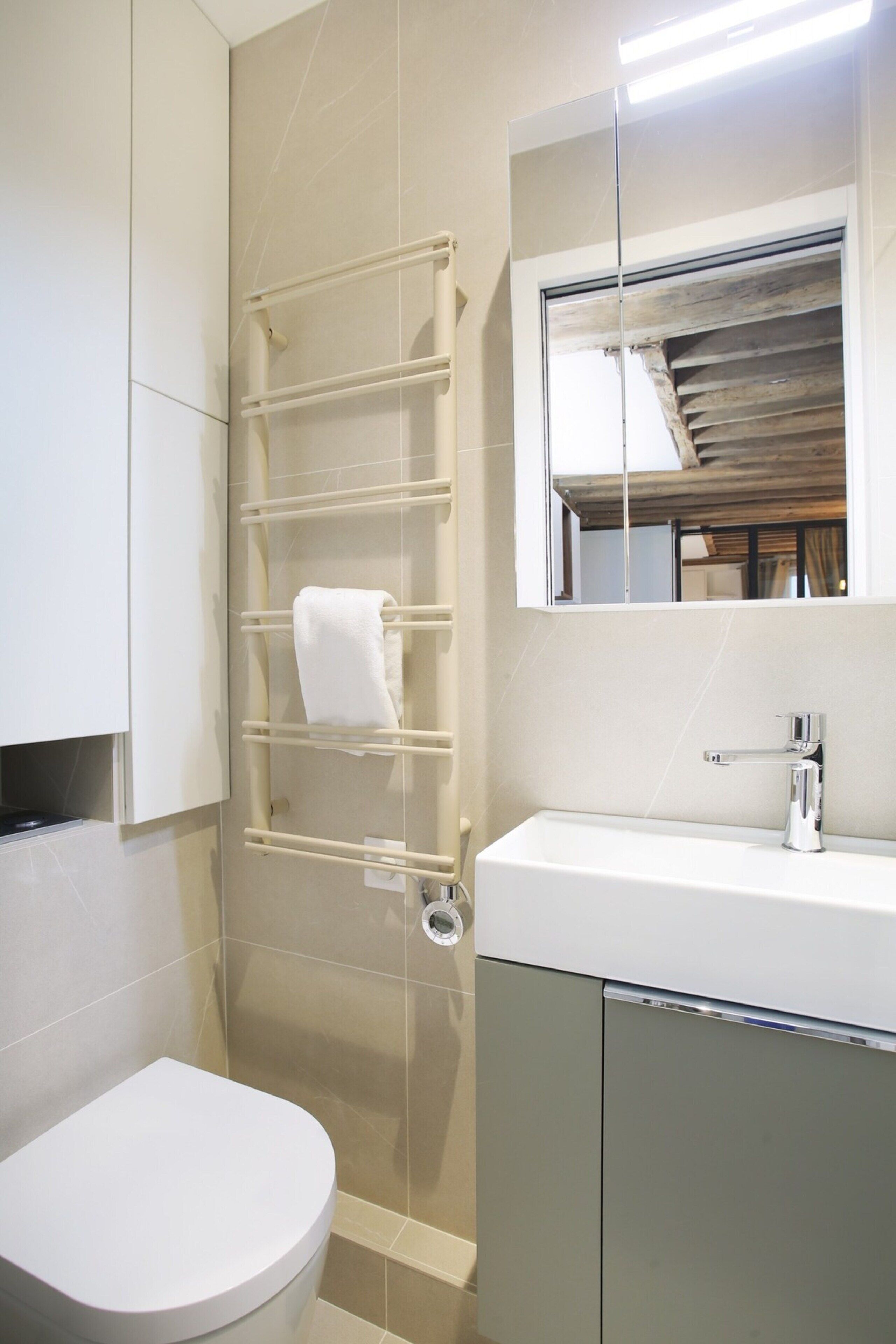 A bathroom with a toilet, a sink, a mirror, and a towel rack.
