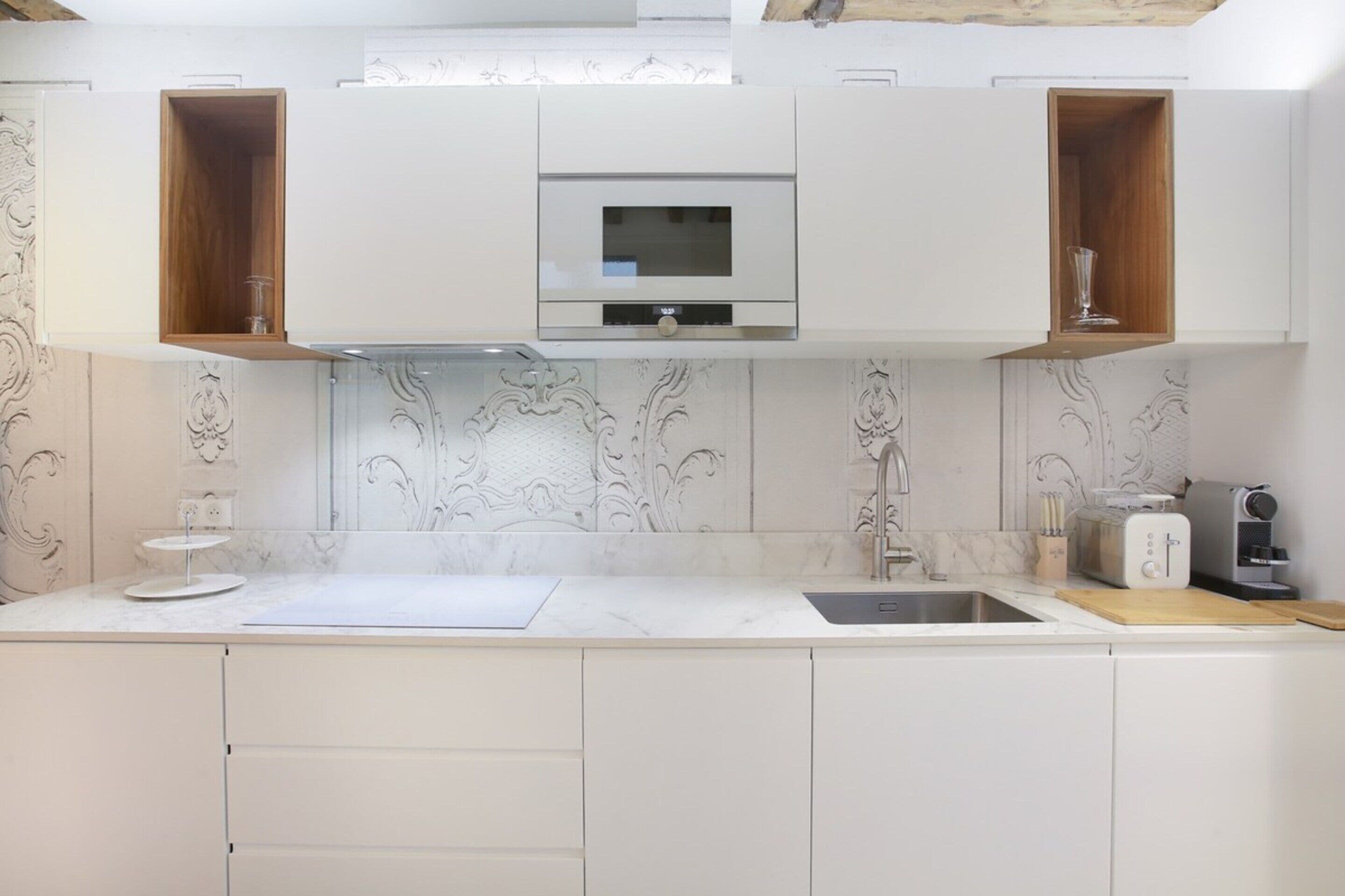 A modern kitchen with white cabinetry, a built-in microwave, and a sink.